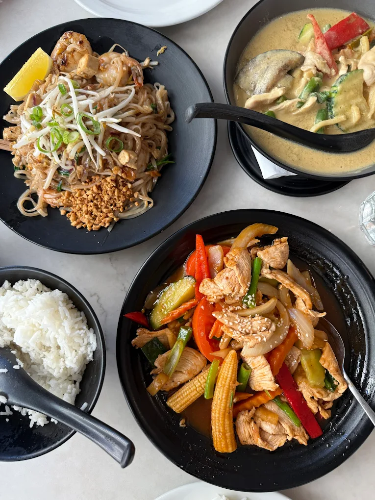 Alt: A table of Thai dishes at Cocohut Thai Restaurant Surfers Paradise, featuring Pad Thai, Green Chicken Curry, Roast Duck Curry, Golden Fried Chicken Wings, and Whole Fried Barramundi